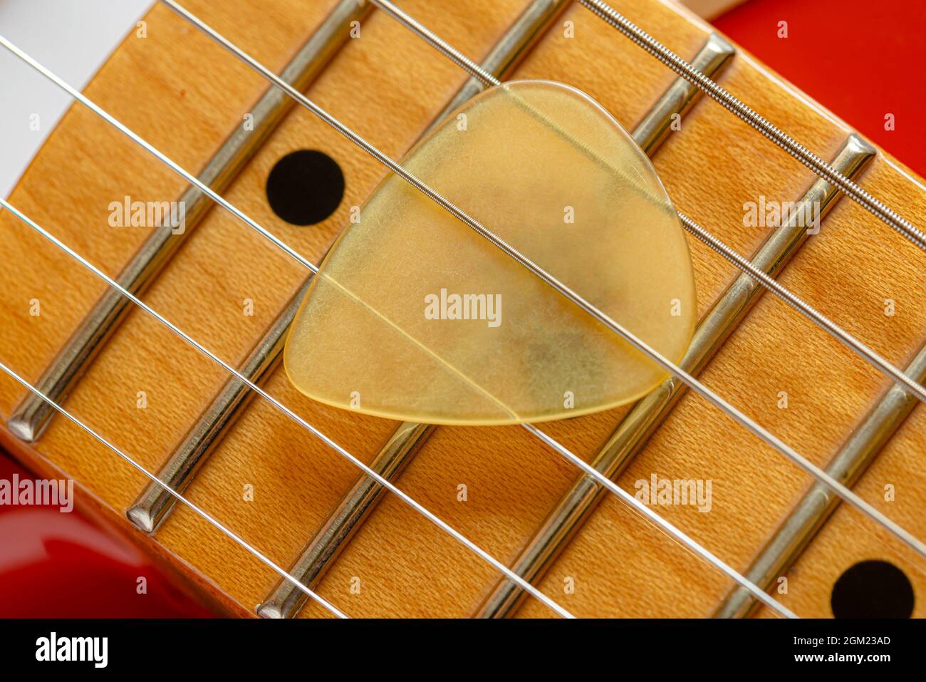 Detail of the neck and the strings of a red electric guitar, with a yellow plectrum also called mediator Stock Photo