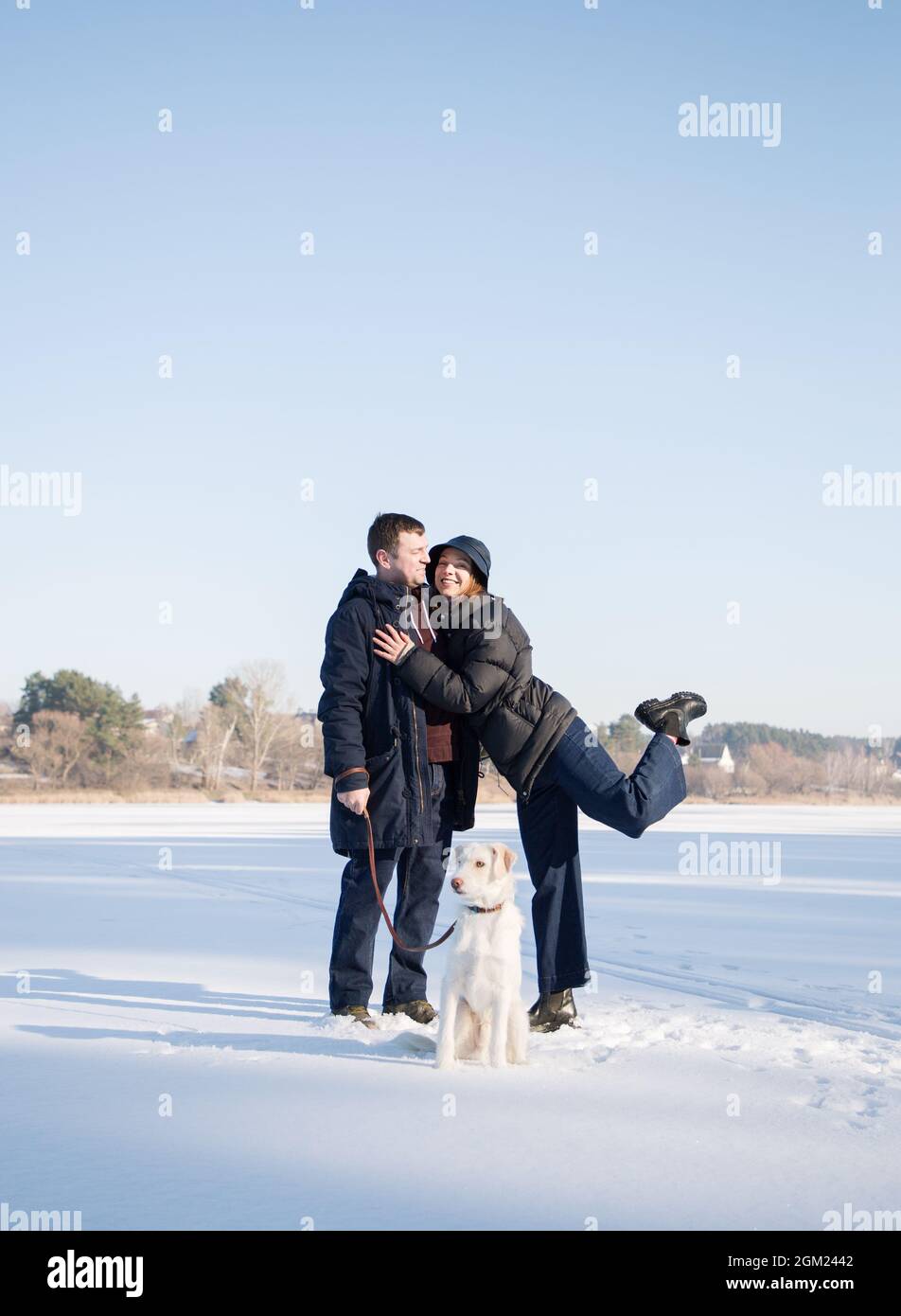 enamored happy man and woman hug, walk the dog in the snow in winter. tender feelings, festive mood, joy of relationship. Valentine's day together Stock Photo