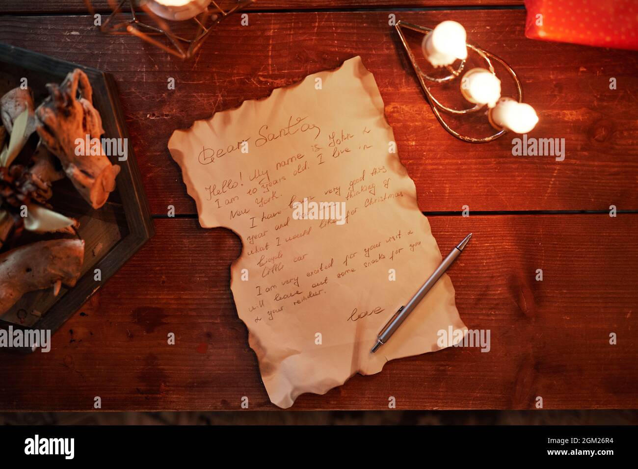 Directly above view of old letter with burnt edges, pen, candles on vintage wooden table Stock Photo