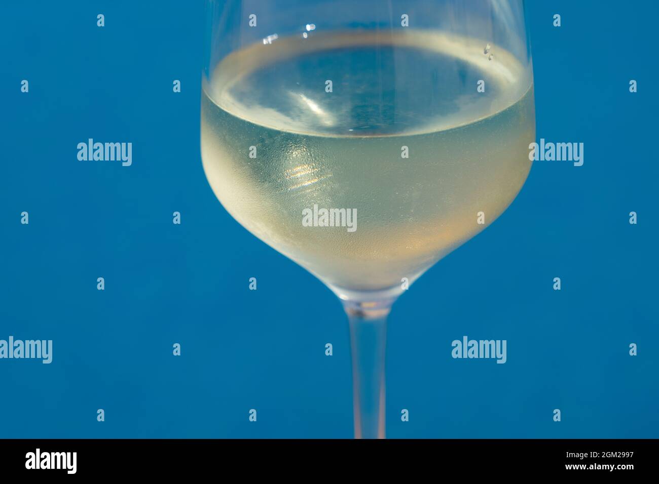 close-up of a wineglass filled with white wine by the blue water for celebration and romance Stock Photo