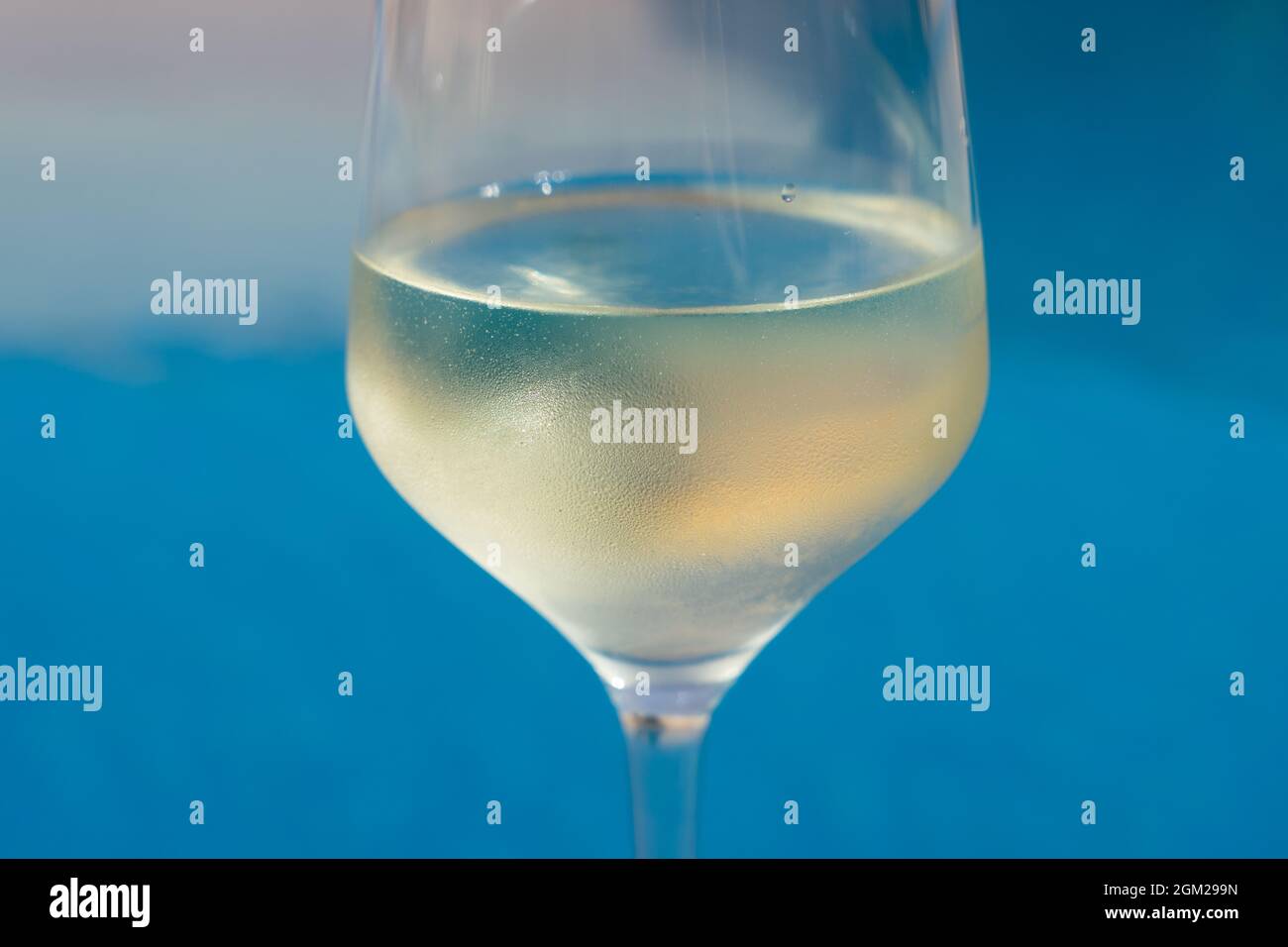 close-up of a wineglass filled with white wine by the blue water for celebration and romance Stock Photo