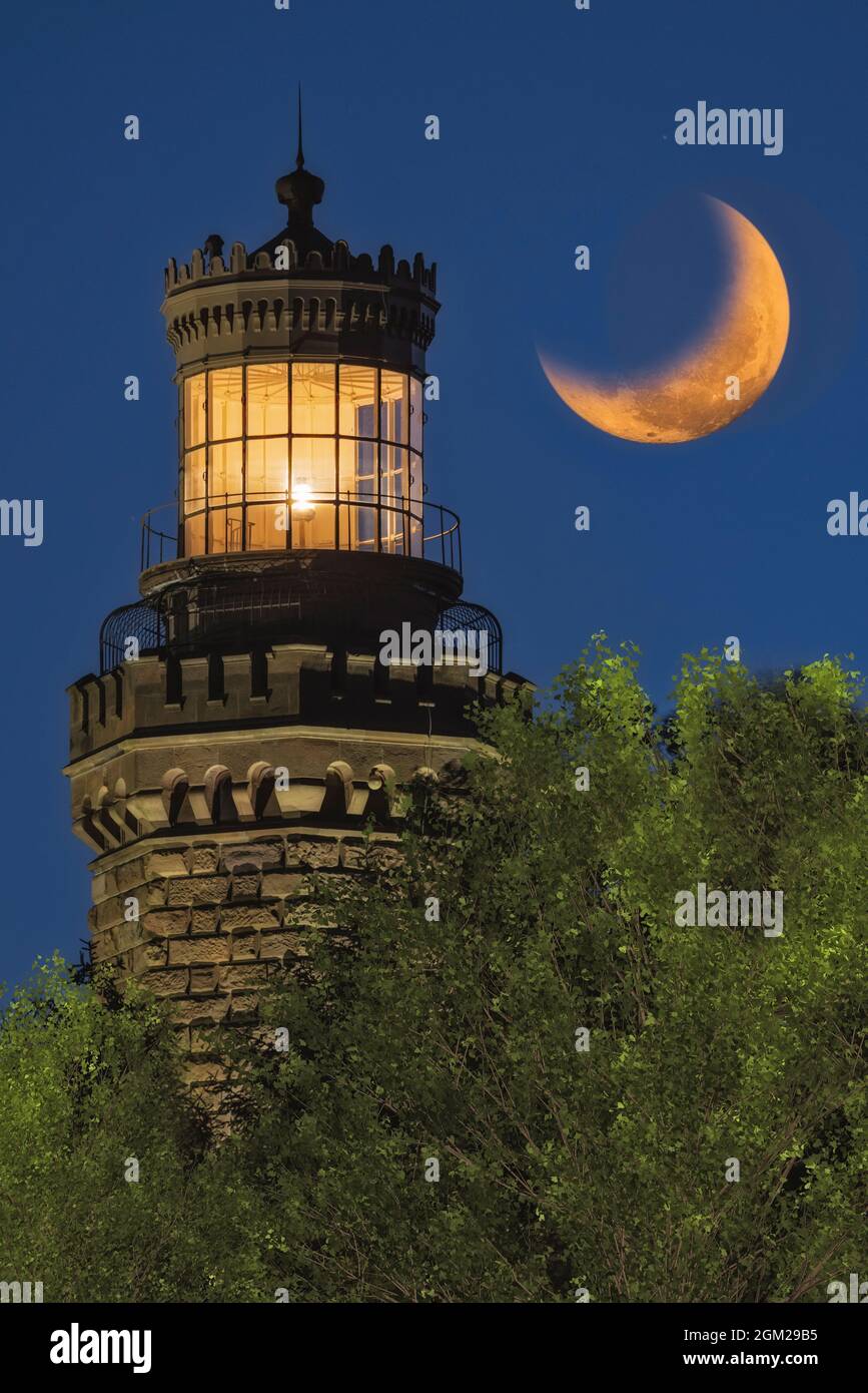 Navesink Twin Lights - Close view to one of the illuminated Lighthouse with the setting moon alongside.  The current lighthouse was constructed in 186 Stock Photo
