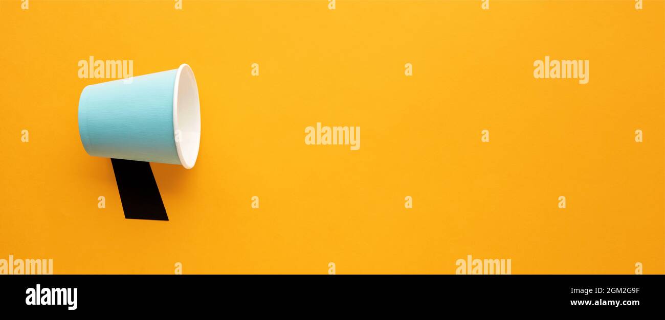 Blue paper cup used as a megaphone on yellow background with copy space ...