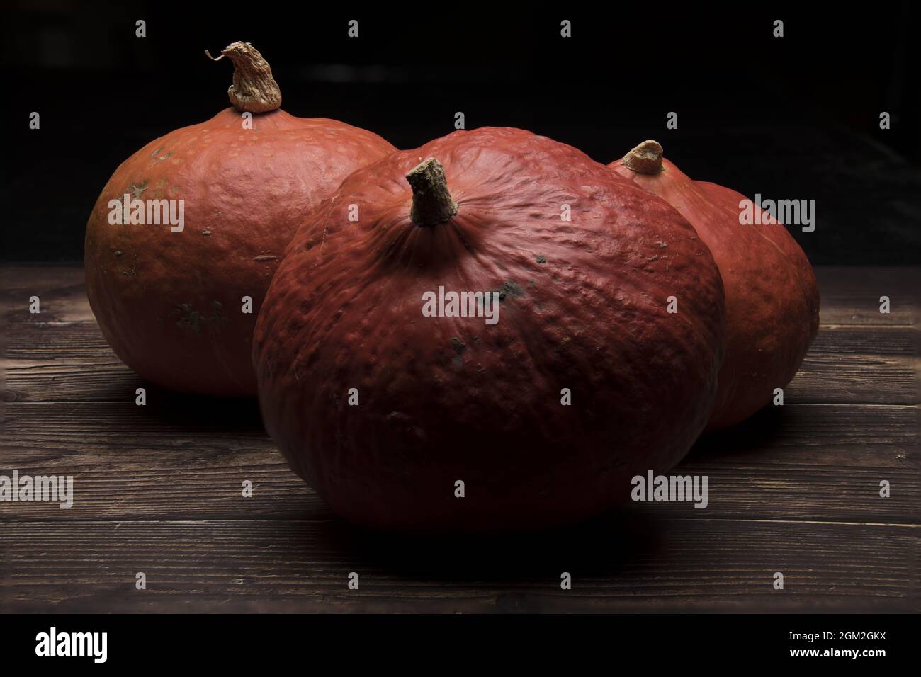 three pumpkins on dark wood against a black background Stock Photo - Alamy