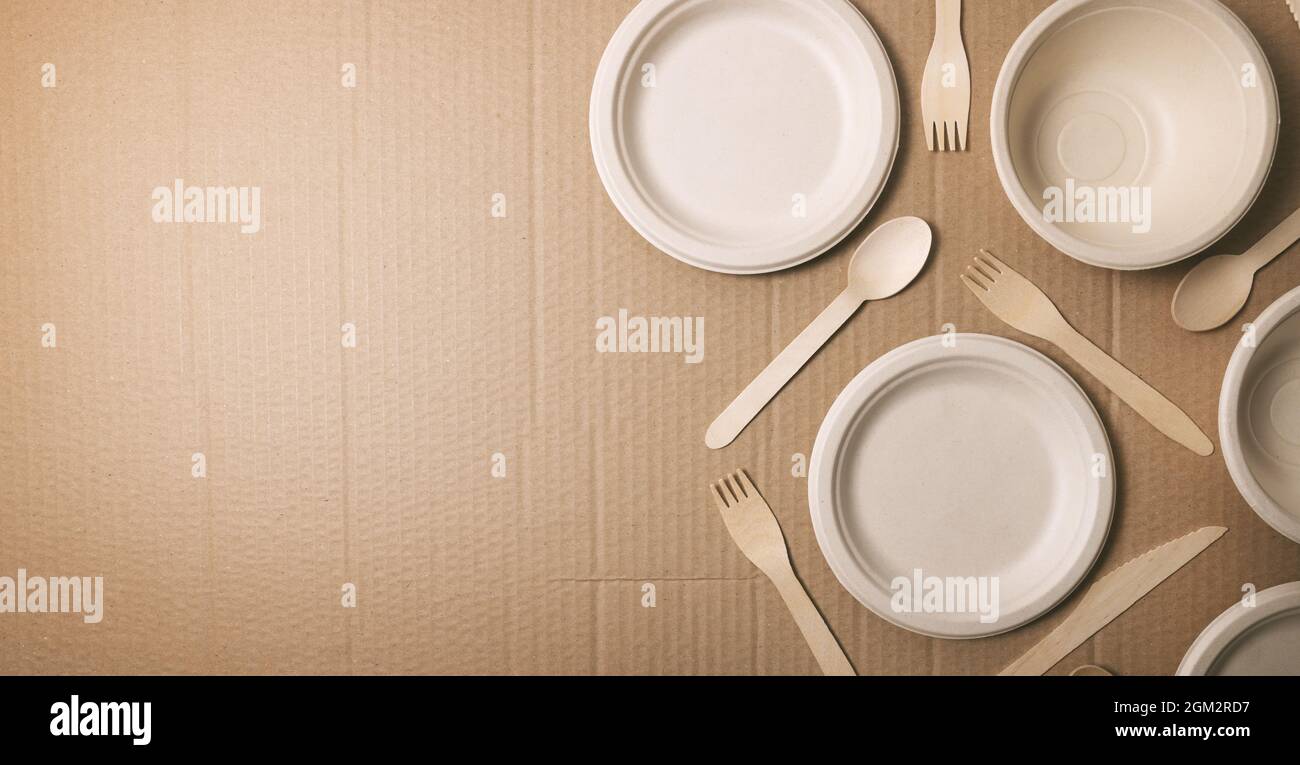 eco friendly disposable tableware. paper dishes and wooden cutlery on cardboard background. copy space Stock Photo