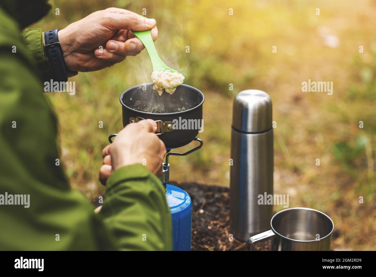 preparing oatmeal porridge outdoors on gas burner. camping cooking equipment Stock Photo