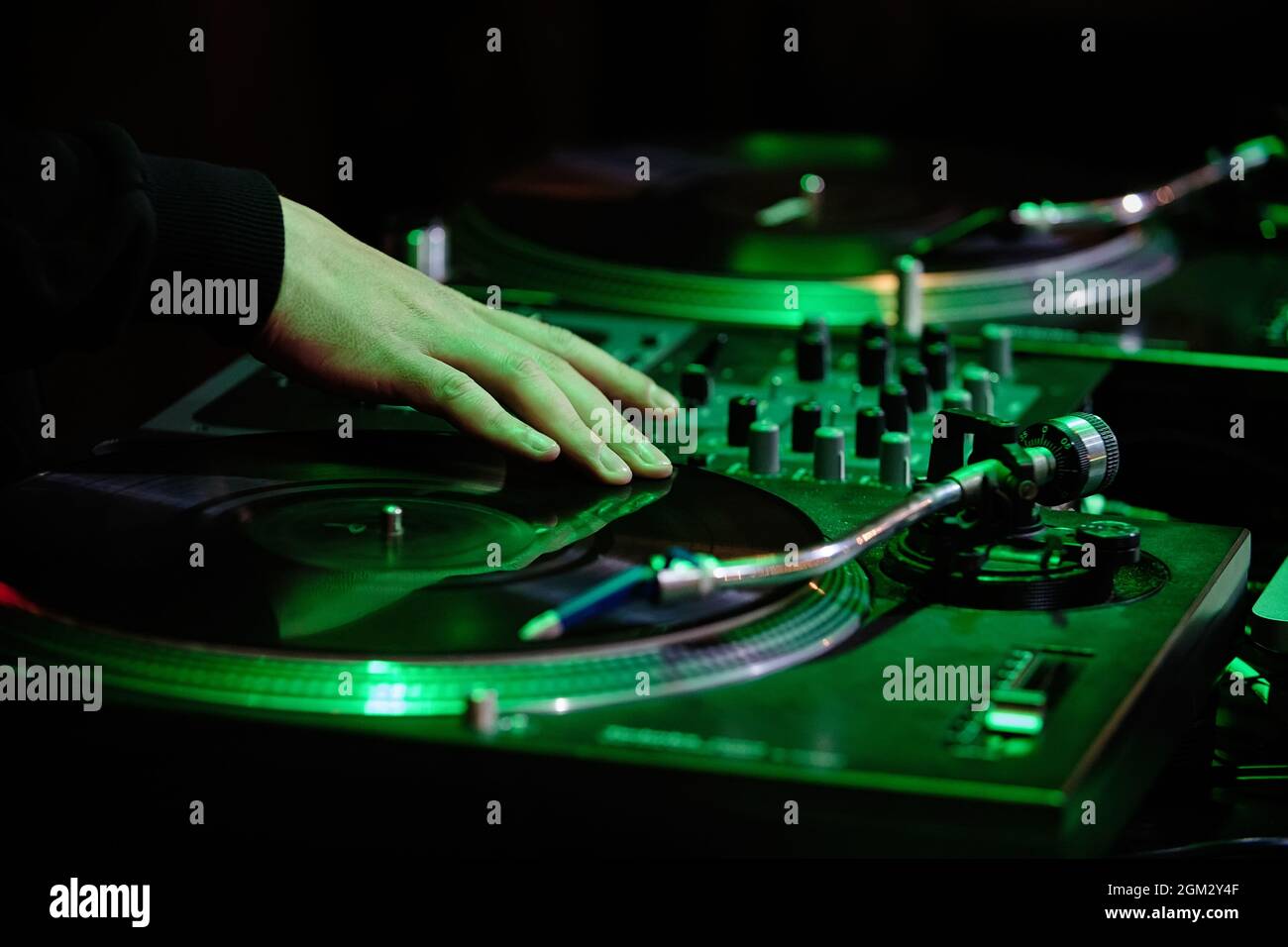 Hand of hip hop dj scratching vinyl record on turntables in green neon