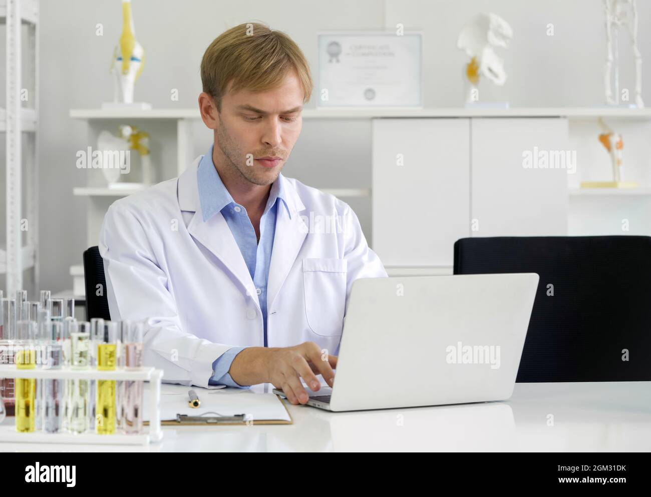 Young caucasian scientist use computers to research chemical compounds on the internet. Working atmosphere in chemical laboratory. Test tubes filled w Stock Photo