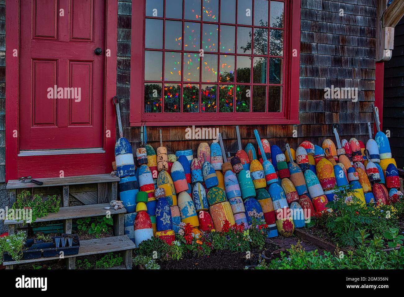 Christmas In Rockport ME - Rows of colorful buoys lined up in a storefront with Motif Number One with a lit up Christmas tree inside at Bradley Wharf Stock Photo
