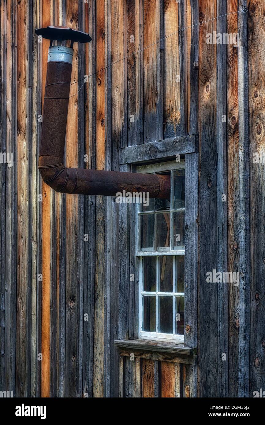 The Way It Was - A rusted exhaust protrudes from a broken window pane against a weathered barn in a rural farmhouse.  This image is available in color Stock Photo