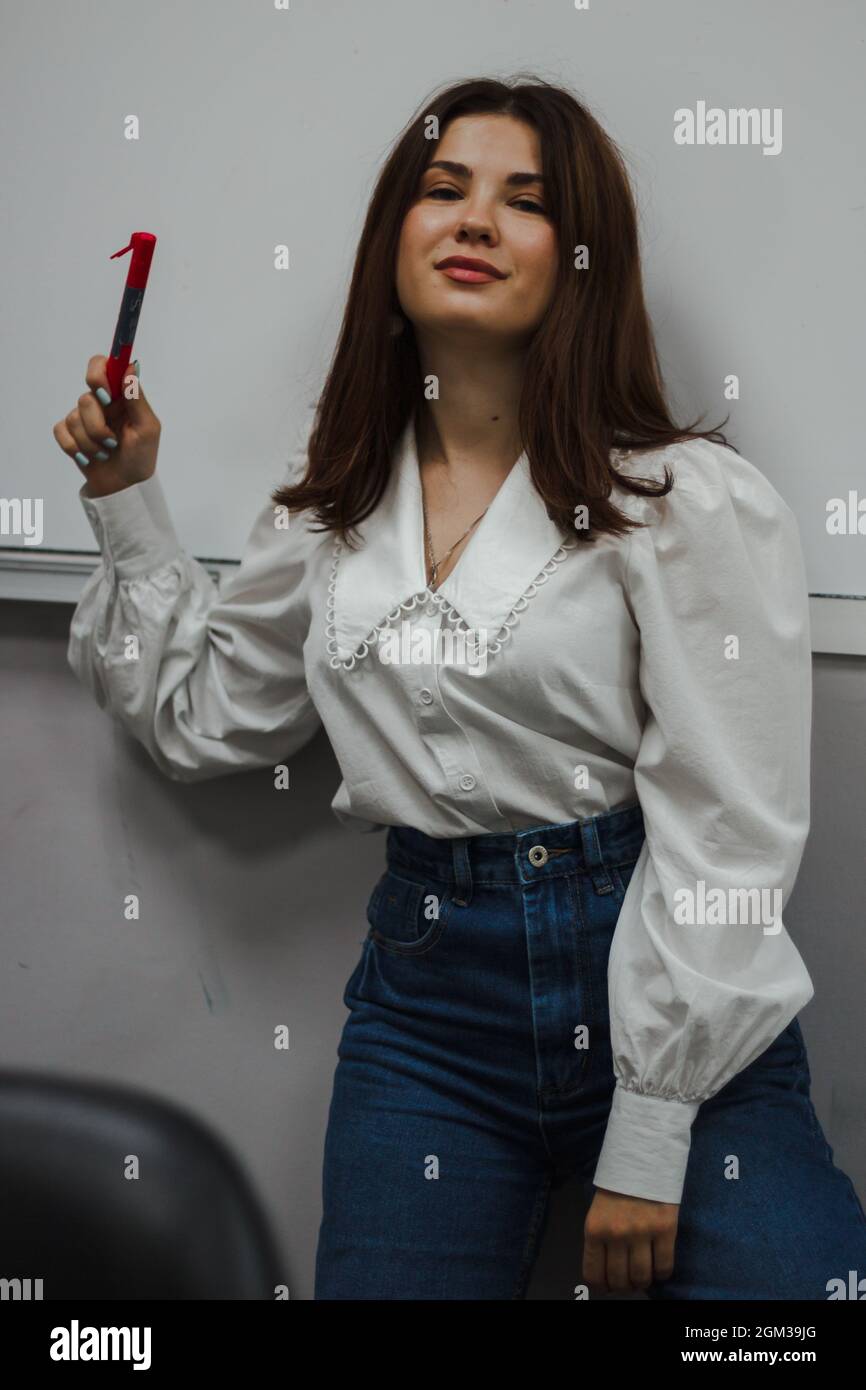 Young eductor in a white blouse with a red marker standing in front of a white board. Looks into the camera. Stock Photo