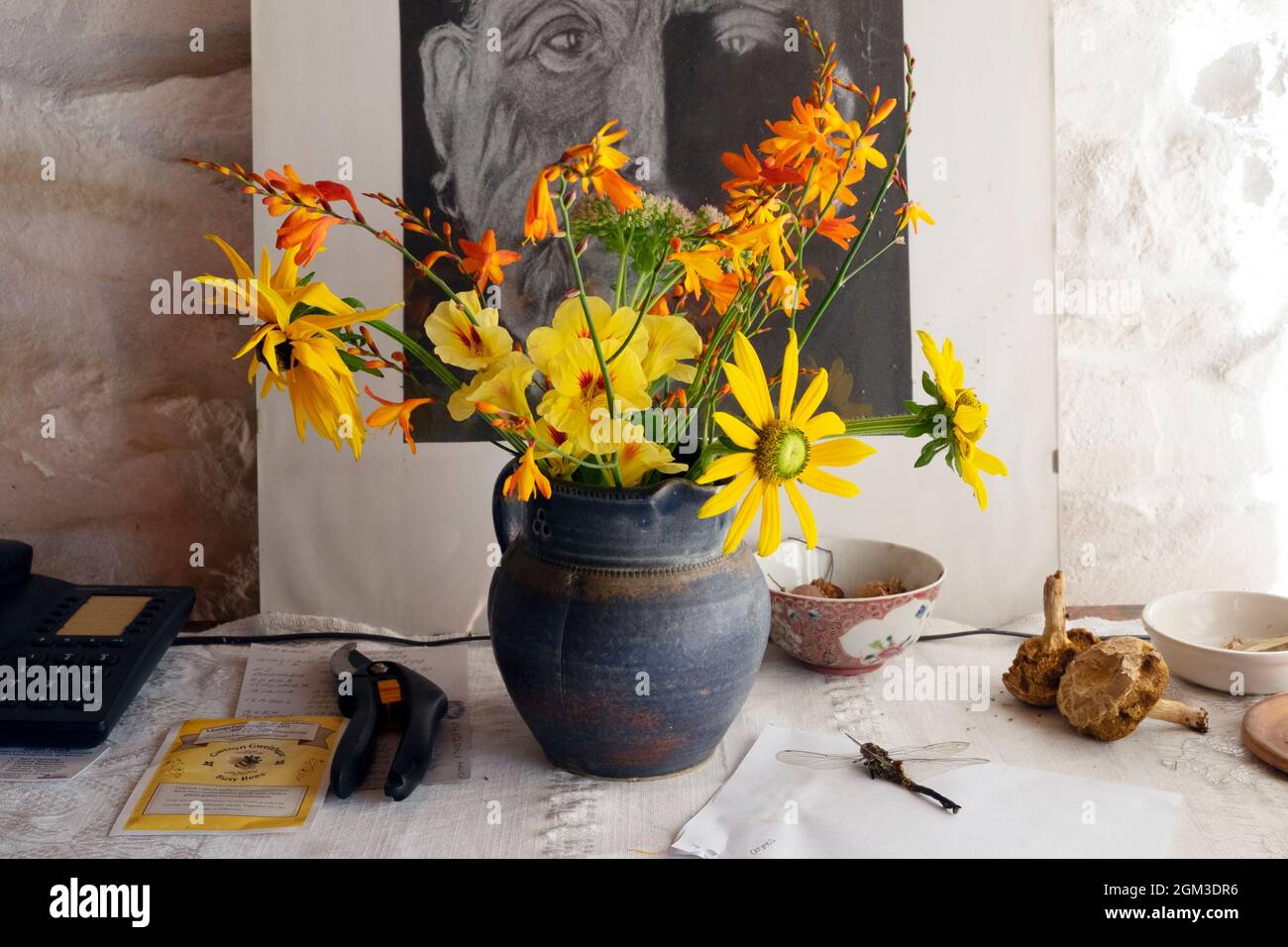 Yellow & orange cut flowers in a blue pottery vase on chest of drawers sideboard with picture secaturs dragonfly home house interior UK KATHY DEWITT Stock Photo