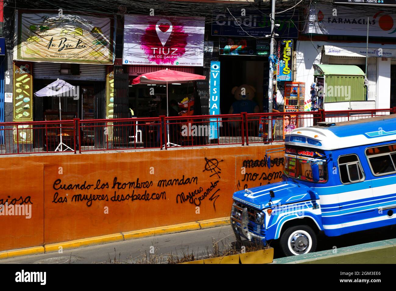 Vintage micro bus driving past feminist graffiti 'When Men Command Women Disobey' by the feminist group Mujeres Creando on orange painted wall, Av 6 de Agosto, La Paz, Bolivia Stock Photo