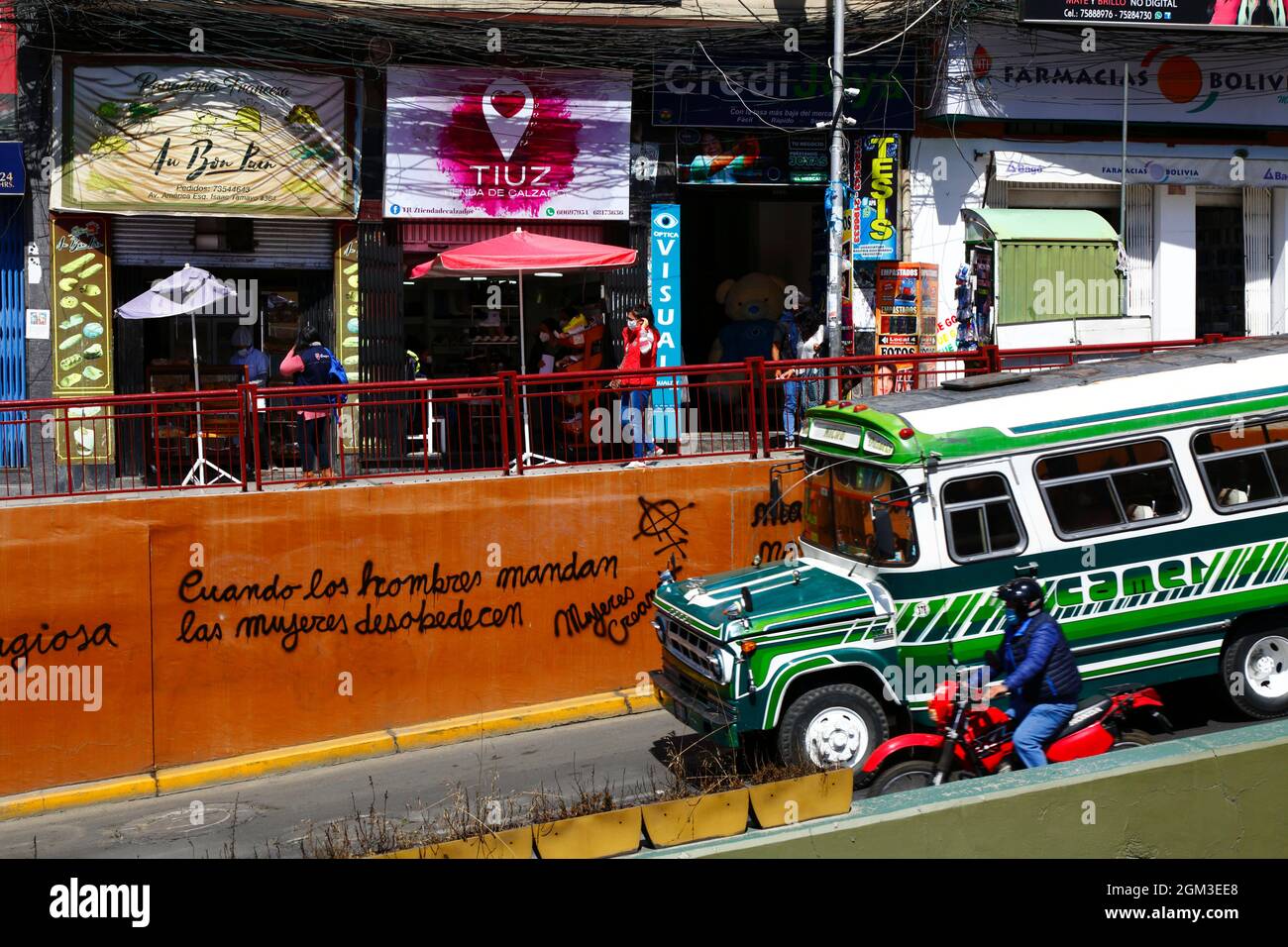 Vintage micro bus driving past feminist graffiti 'When Men Command Women Disobey' by the feminist group Mujeres Creando on orange painted wall, Av 6 de Agosto, La Paz, Bolivia Stock Photo