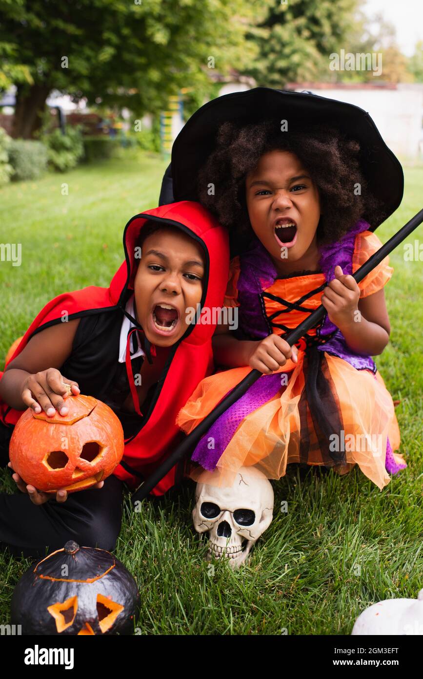 spooky african american kids in halloween costumes screaming while playing on backyard Stock Photo