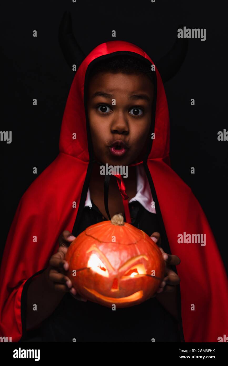 spooky african american boy in devil halloween costume holding carved