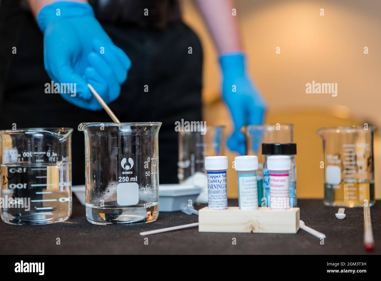 Latex gloved hand pour a beaker of liquid during a science experiment in school lab. Stock Photo