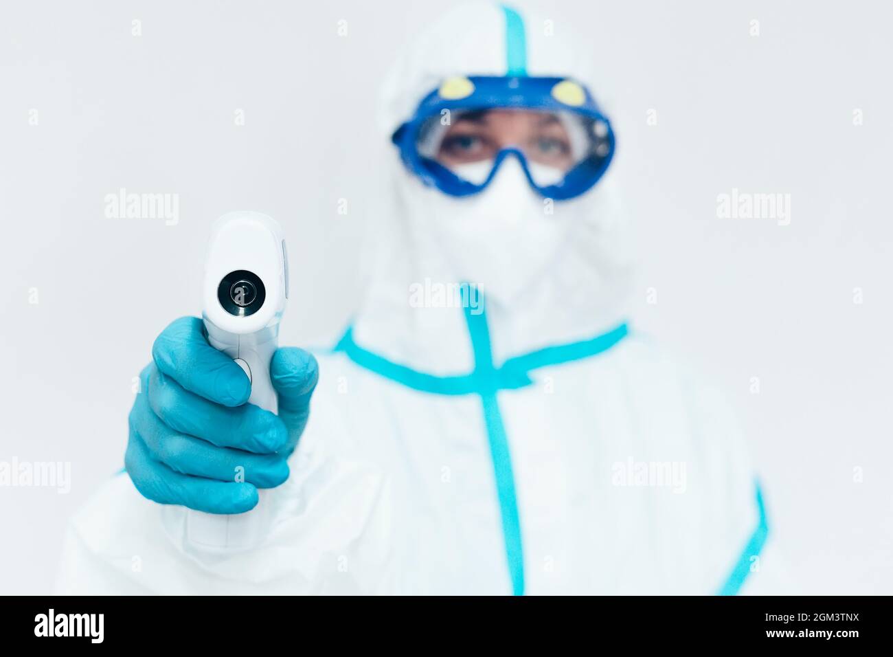 A medic in a protective medical suit and mask holds a modern infrared thermometer in his hand. Measurement of body temperature with a non-contact thermometer. Covid-19 disease control. Stock Photo