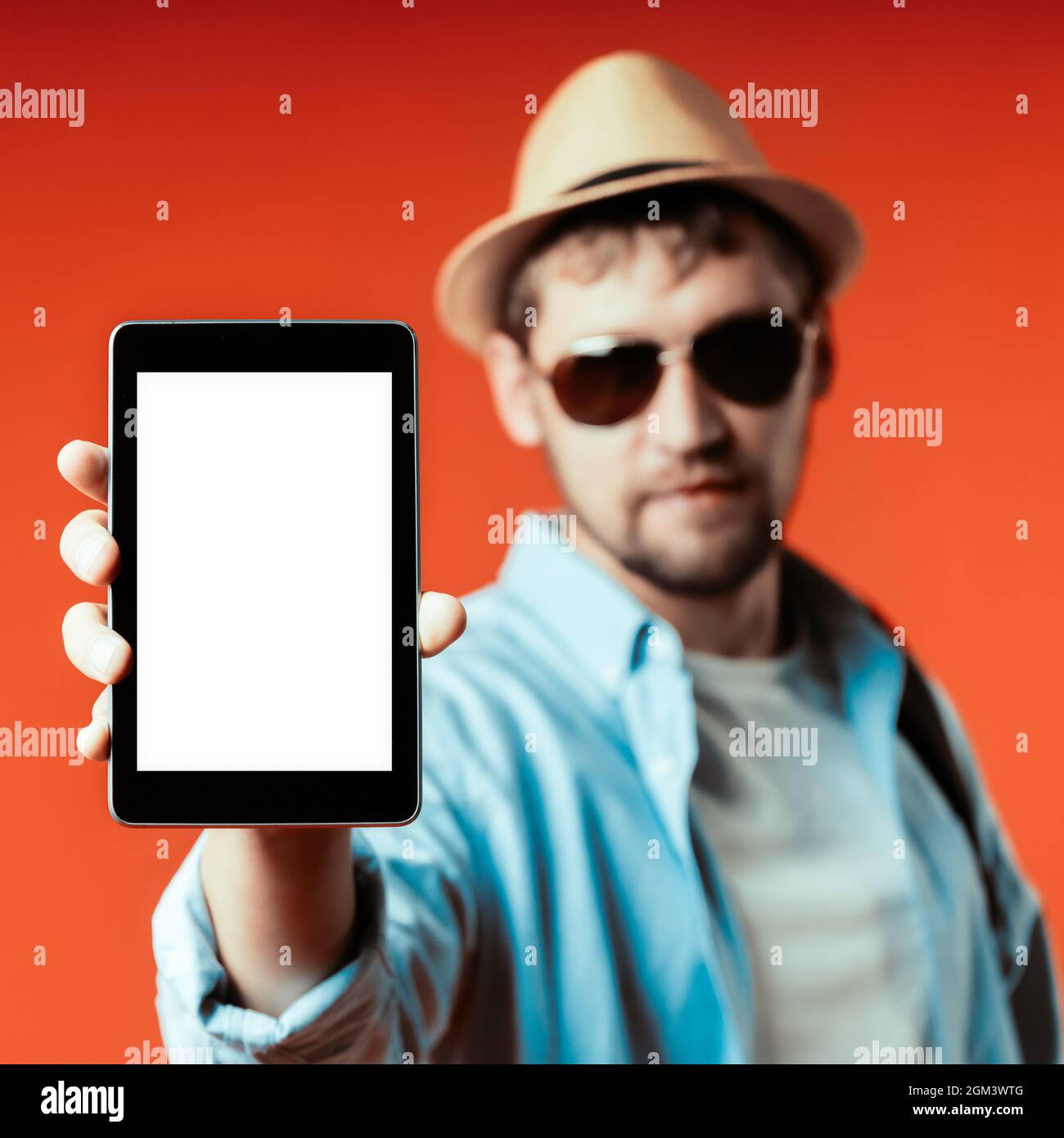 A Caucasian tourist in a hat and sunglasses shows a tablet with a white screen. The concept of a mobile application for travelers. Announcement and promotional offer Stock Photo