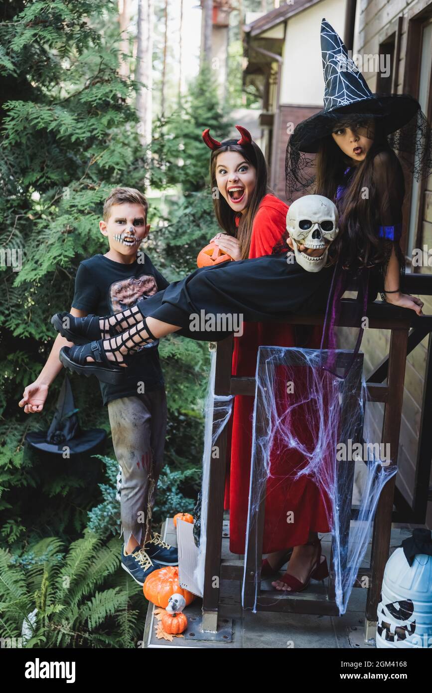 excited kids in spooky halloween costumes grimacing on cottage porch Stock Photo