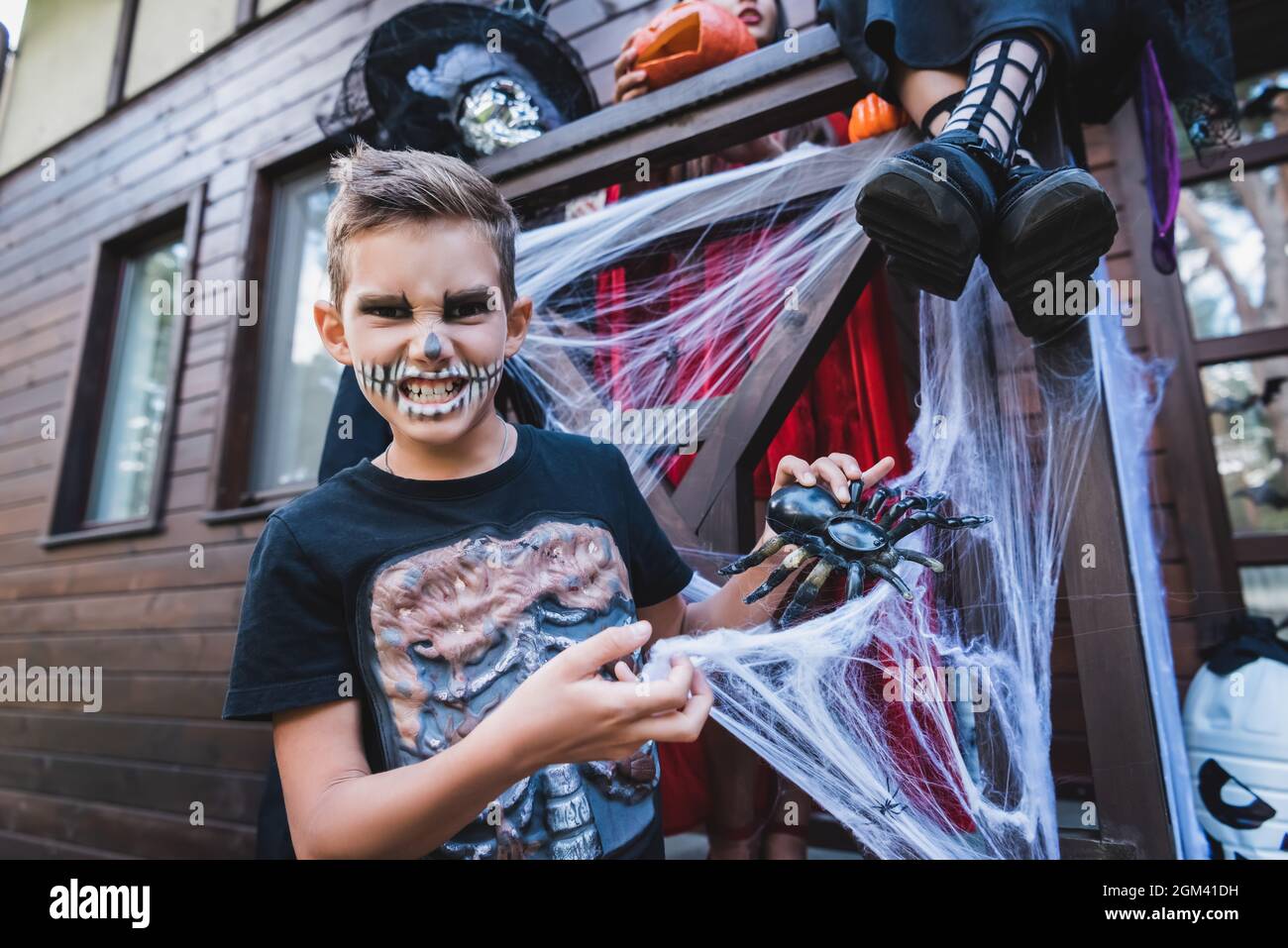 grimacing boy in skeleton costume playing with toy spider near sisters Stock Photo