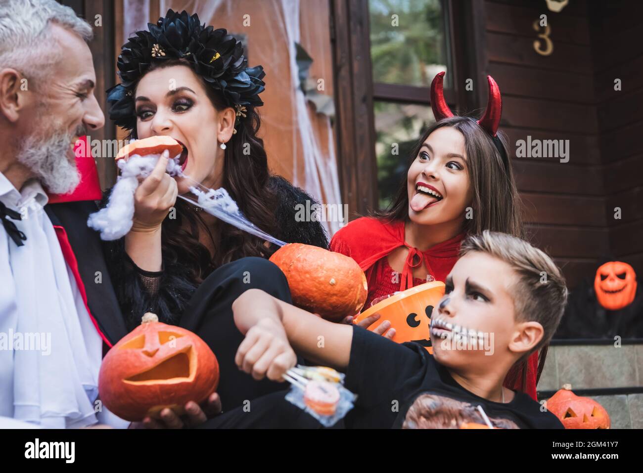 woman eating raw pumpkin near excited family in spooky halloween costumes Stock Photo