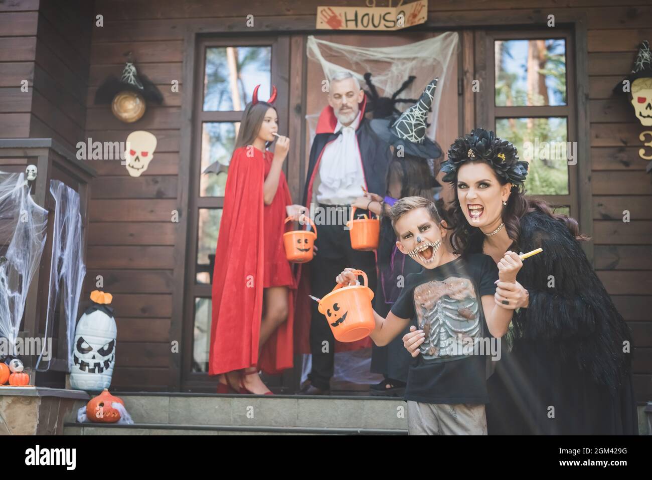 mother and son grimacing near blurred family in halloween costumes on decorated porch Stock Photo