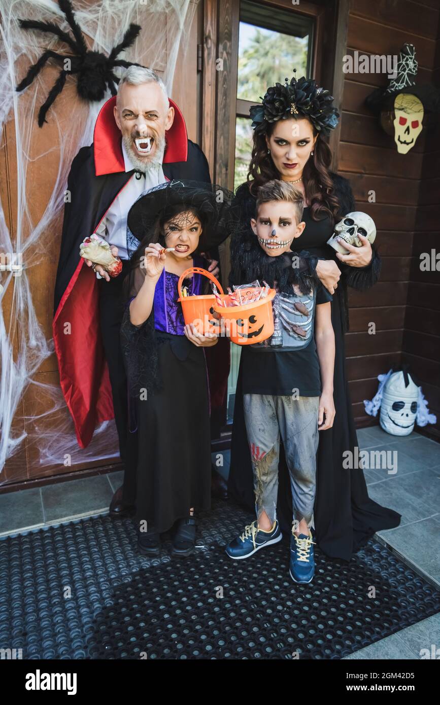 spooky family in halloween costumes grimacing on porch with decoration Stock Photo