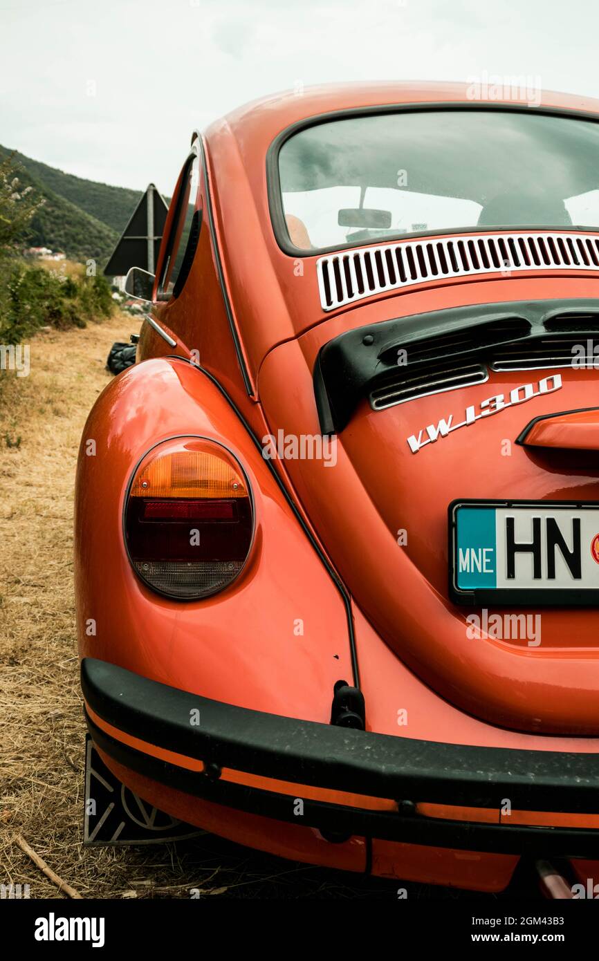 A side shot of an orange Volkswagen Beetle parked on the side of a road on a cloudy day Stock Photo