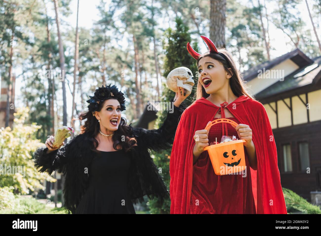 woman in vampire halloween costume screaming and scaring daughter with skull and toy hand Stock Photo