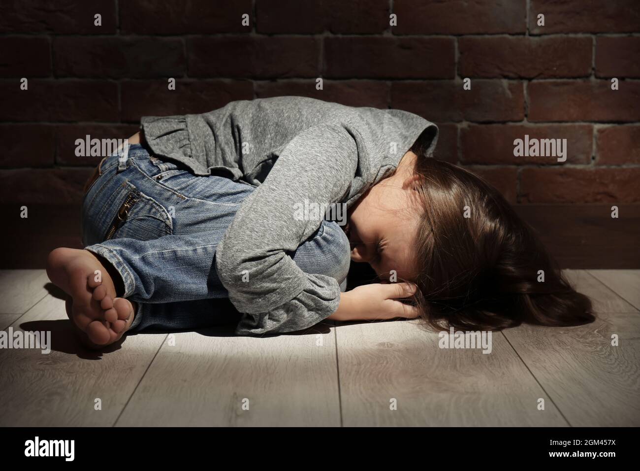 Helpless little girl lying on floor against brick wall. Abuse of