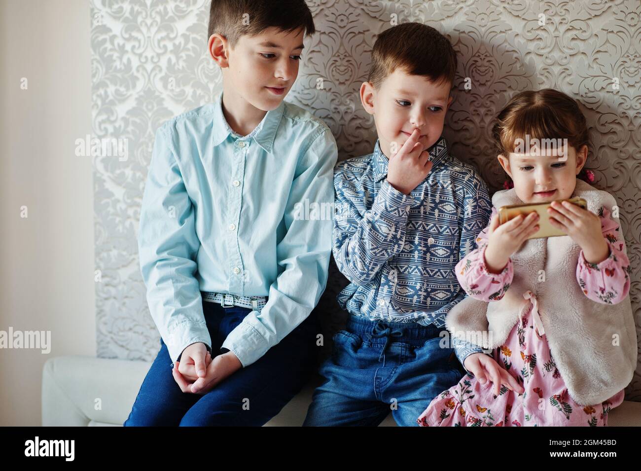 Three kids. Girl with mobile phone at hand. Stock Photo