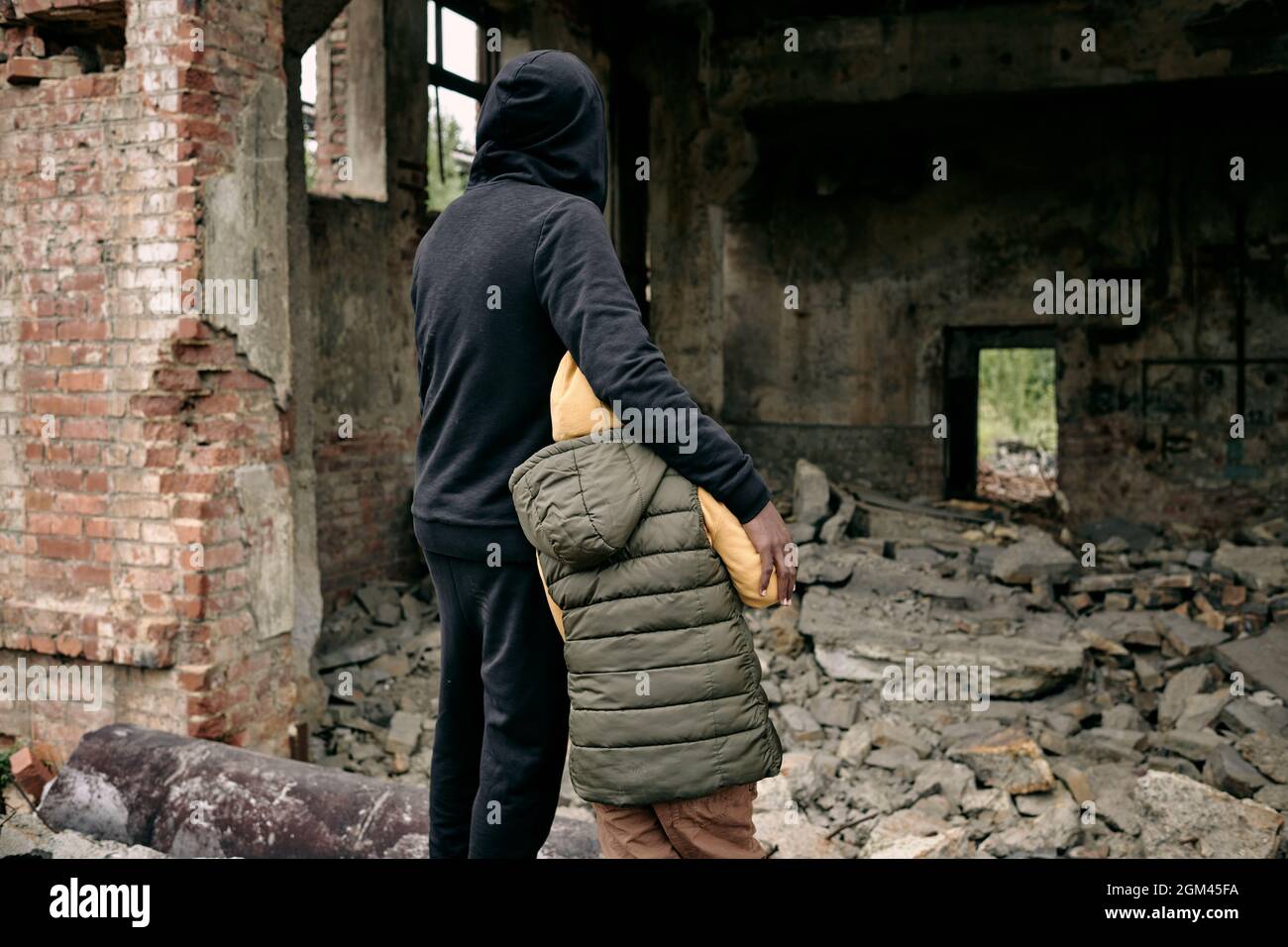 Rear view of father embracing child and looking at ruins of house after hostilities Stock Photo