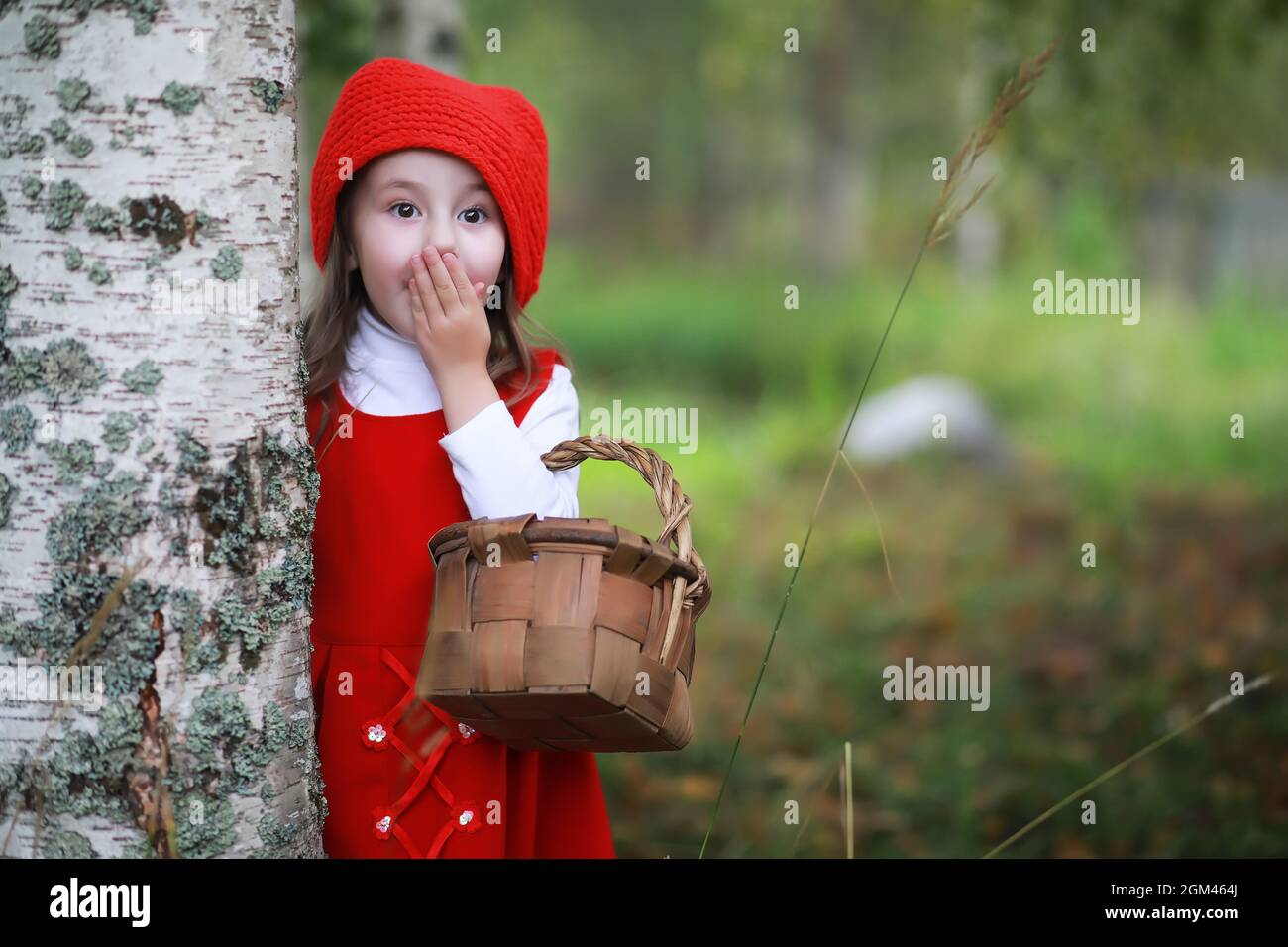 A little girl in a red hat and dresses is walking in the park. Cosplay ...
