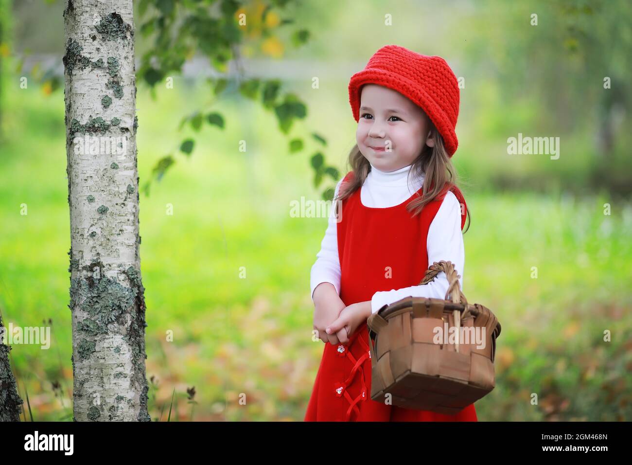 A little girl in a red hat and dresses is walking in the park. Cosplay ...
