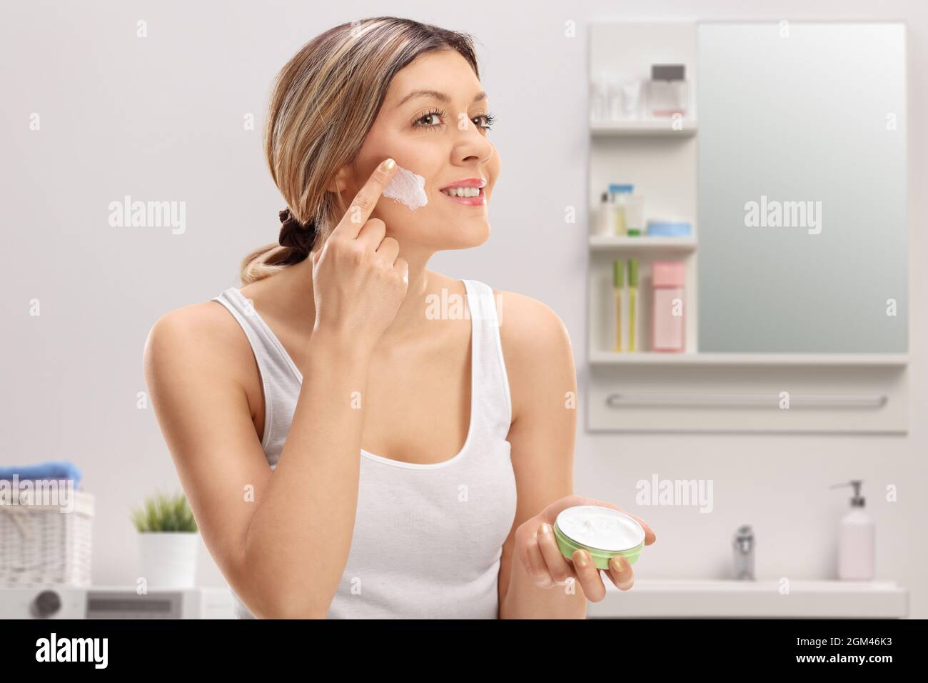 Young woman applying face cream inside a bathroom Stock Photo