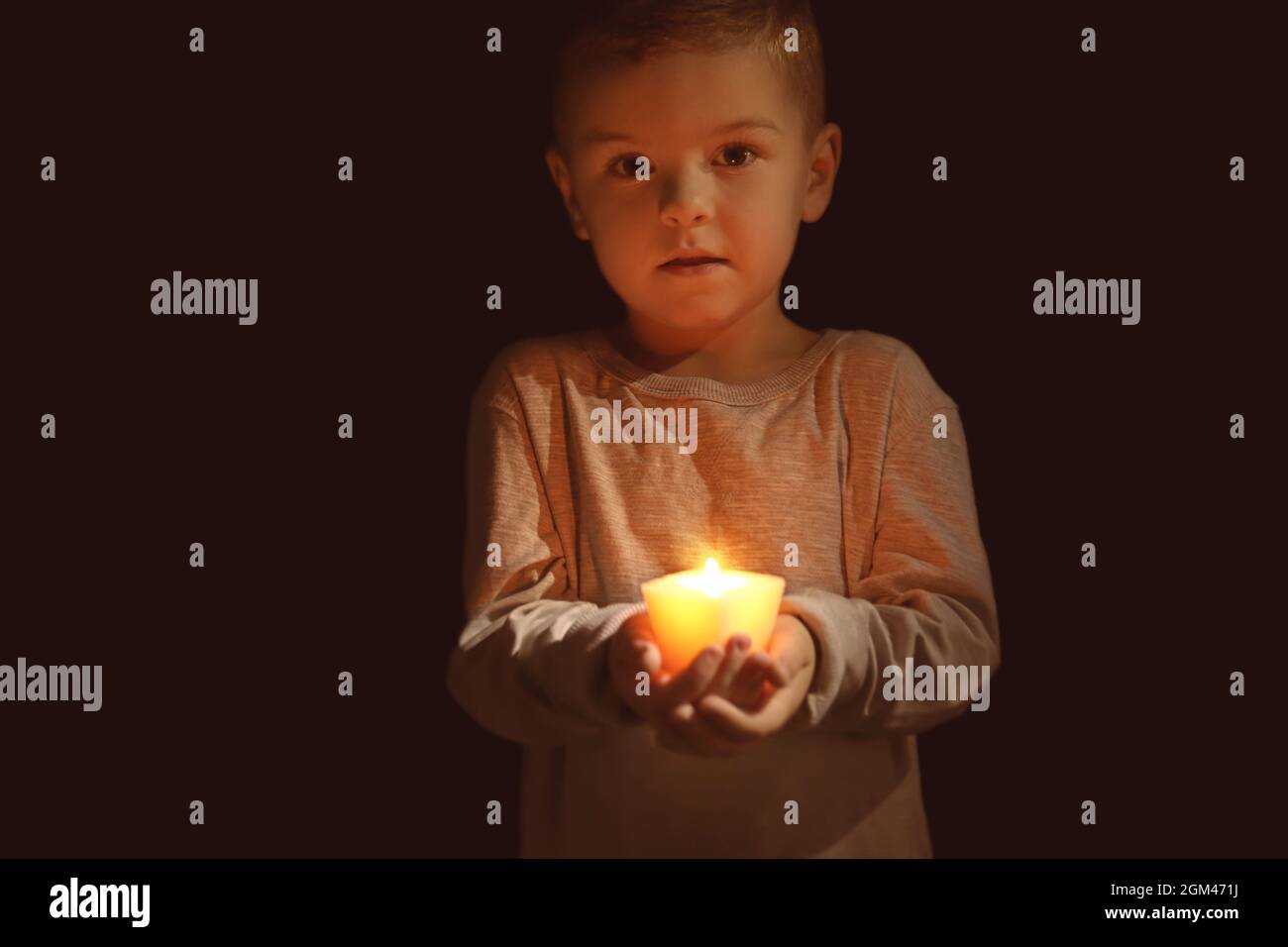 Little boy holding burning candle in darkness Stock Photo Alamy