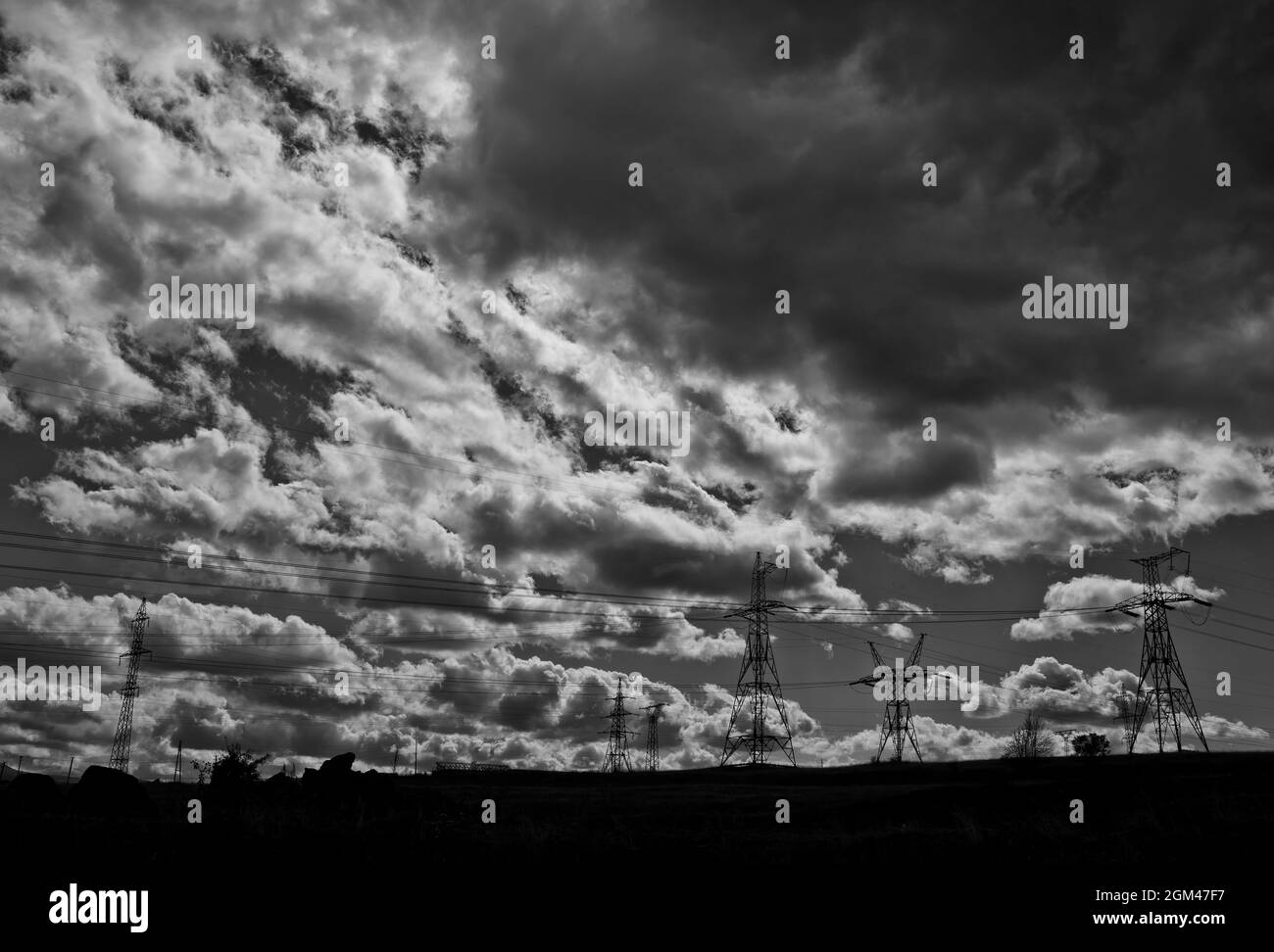 Grayscale shot of transmission towers under the sunlight and a cloudy sky Stock Photo