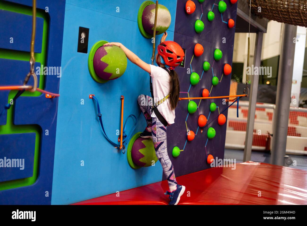 Girl wearing in harness and safety equipment climbing on practical wall