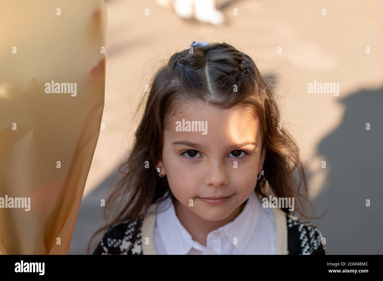 Smiling little girl with long dark hair in a white blouse and a plaid jacket holding a bouquet of flowers in her hand. First-grader's first bell at sc Stock Photo