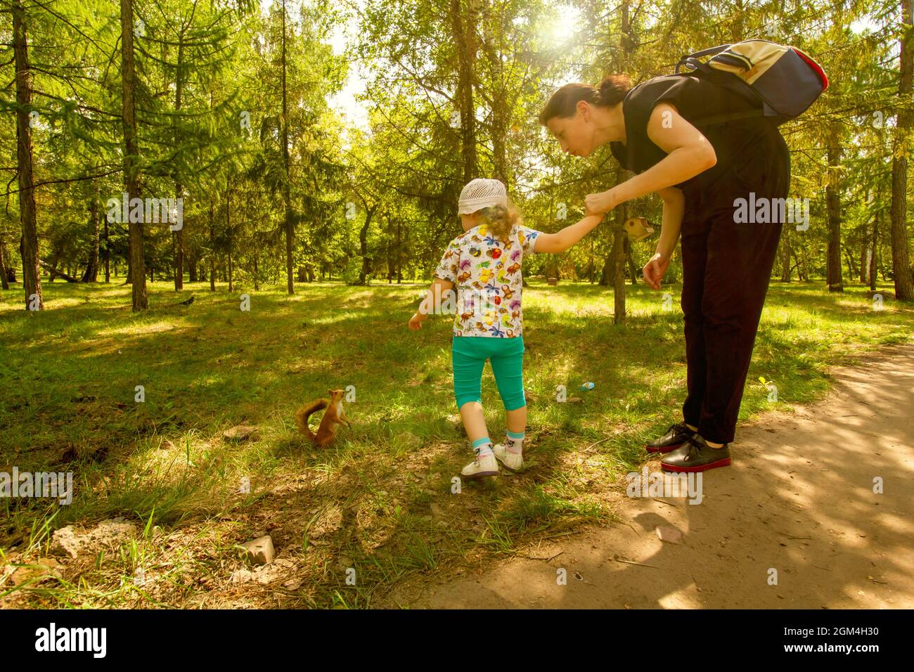 Mom and daughter are playing with a squirrel in the forest. Stock Photo