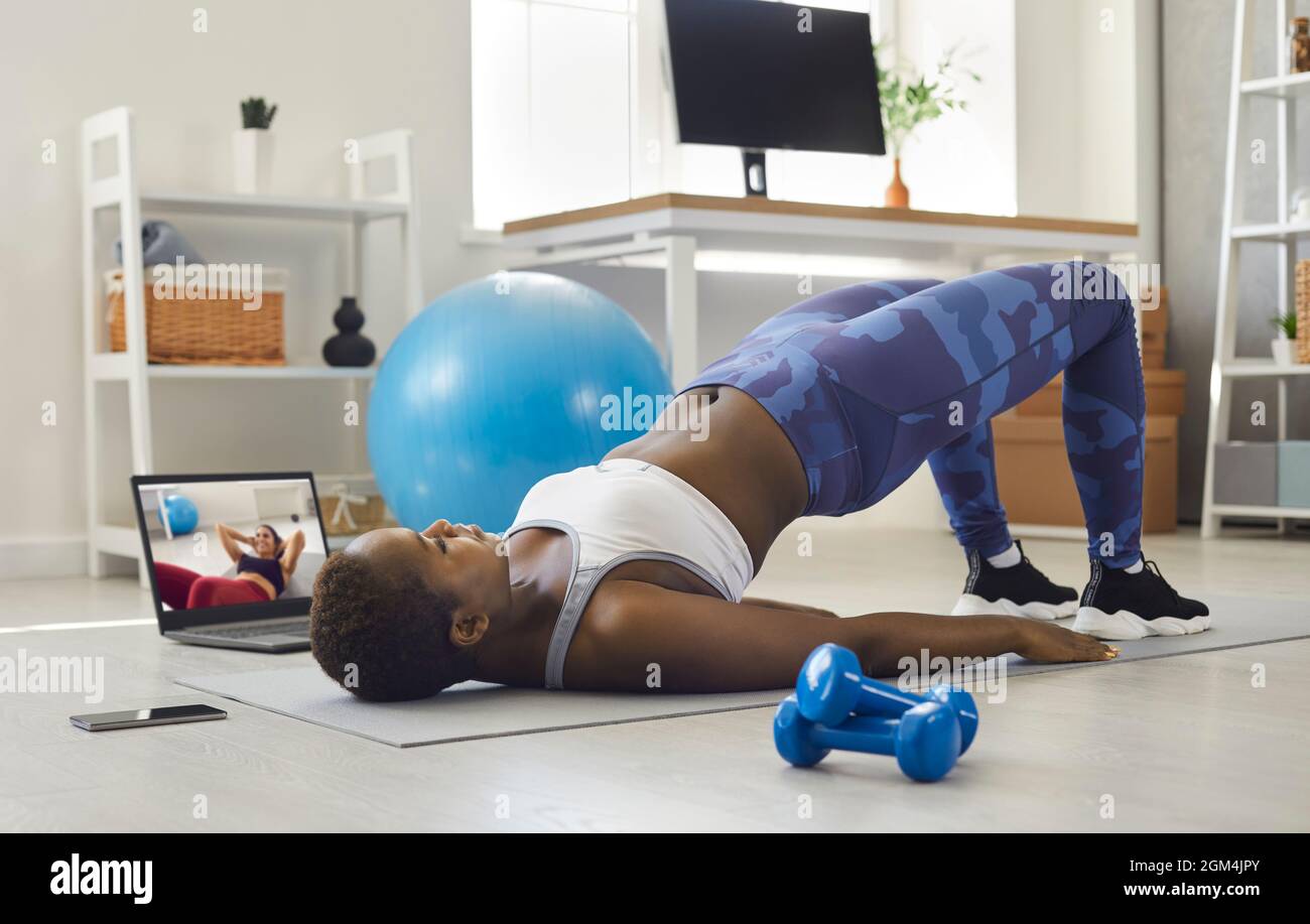Black woman watching sports workout video and doing glute bridge exercise at home Stock Photo Alamy