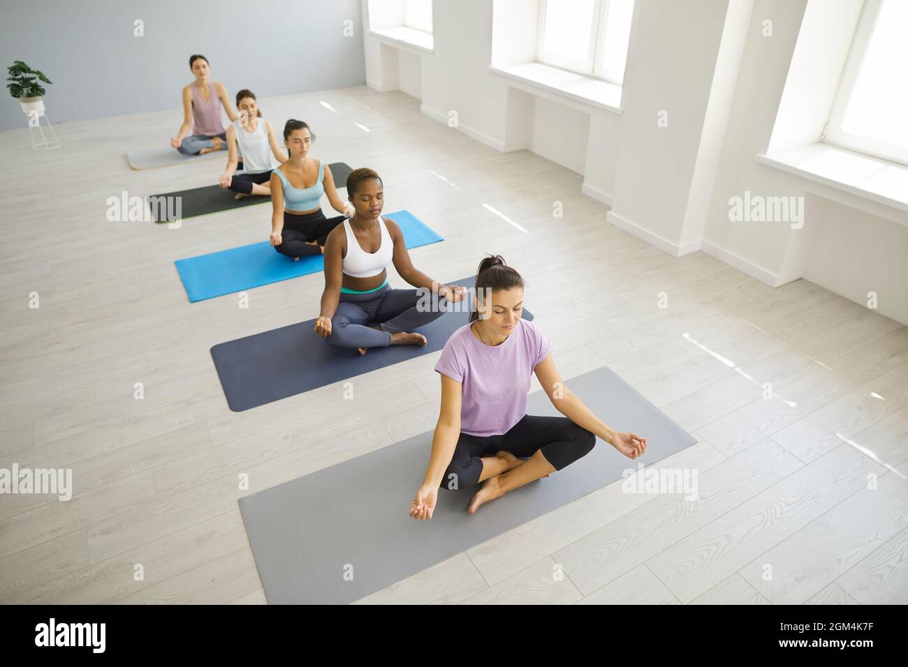 Group of relaxed ladies doing breathing exercise and meditating on yoga mats at gym Stock Photo