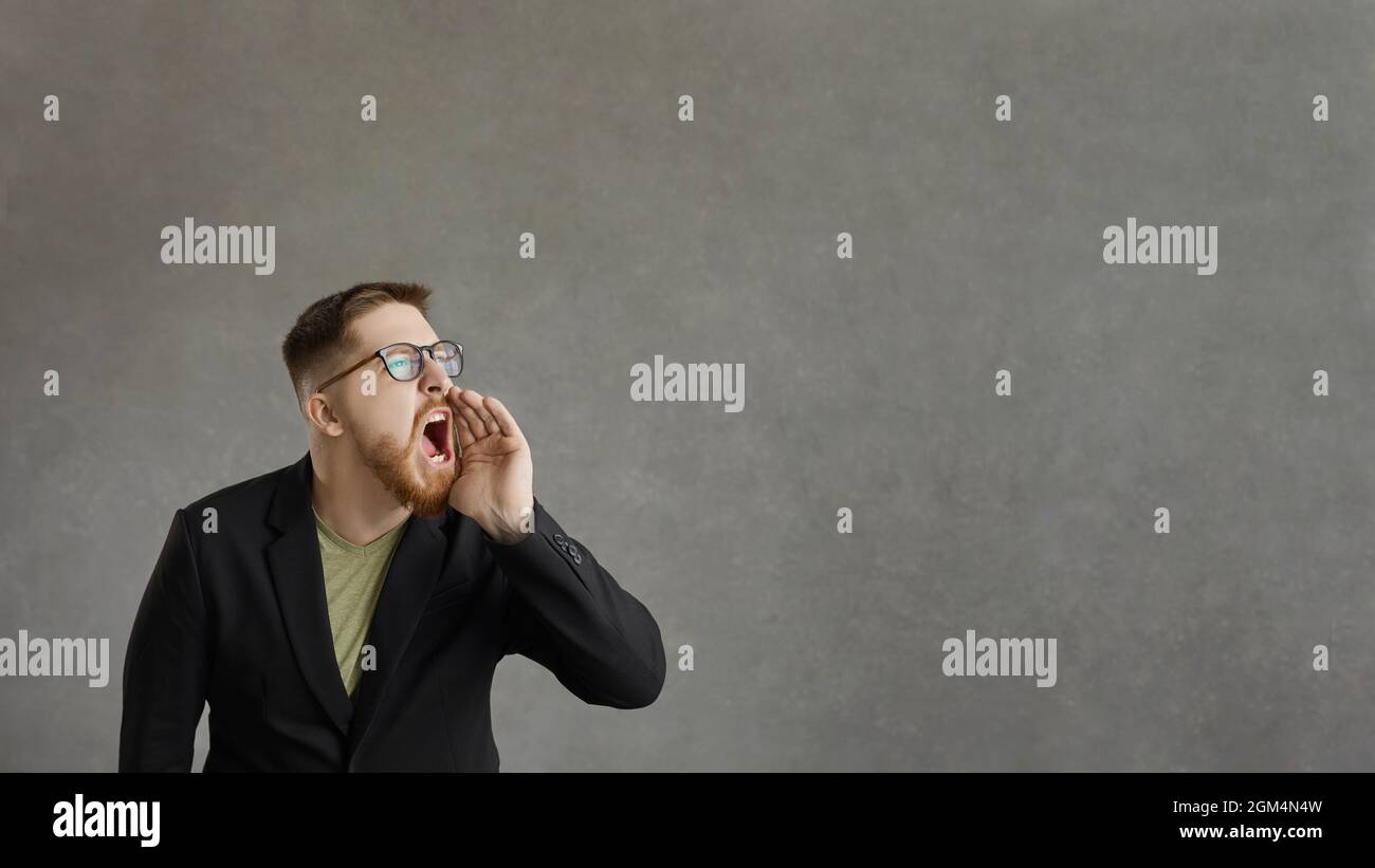 Active man who shouts, announcing advertising information standing on a gray background. Stock Photo