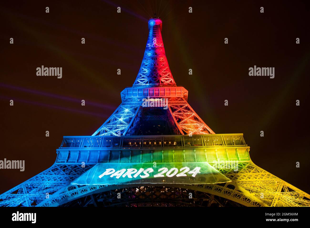 Wide view of the Eiffel Tower lit up in rainbow colors at night and reads Paris 2024 while preparing to host the Olympic Games. Stock Photo