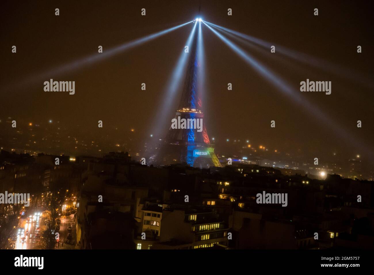 Aerial view of a foggy Eiffel Tower with spotlights and rainbow colors