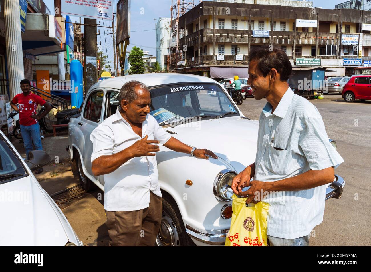 Udupi, Karnataka, India : Two men chat next to a vintage Ambassador car. The Hindustan Ambassador automobile was manufactured by Hindustan Motors of I Stock Photo