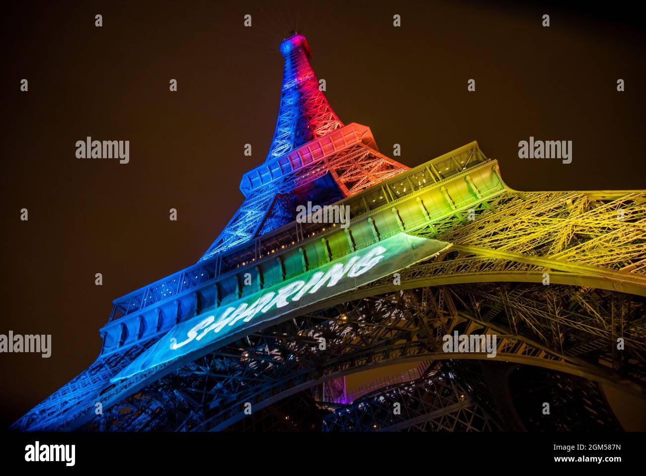 Wide view of the Eiffel Tower lit up in rainbow colors at night and reads Paris 2024 while preparing to host the Olympic Games. Stock Photo