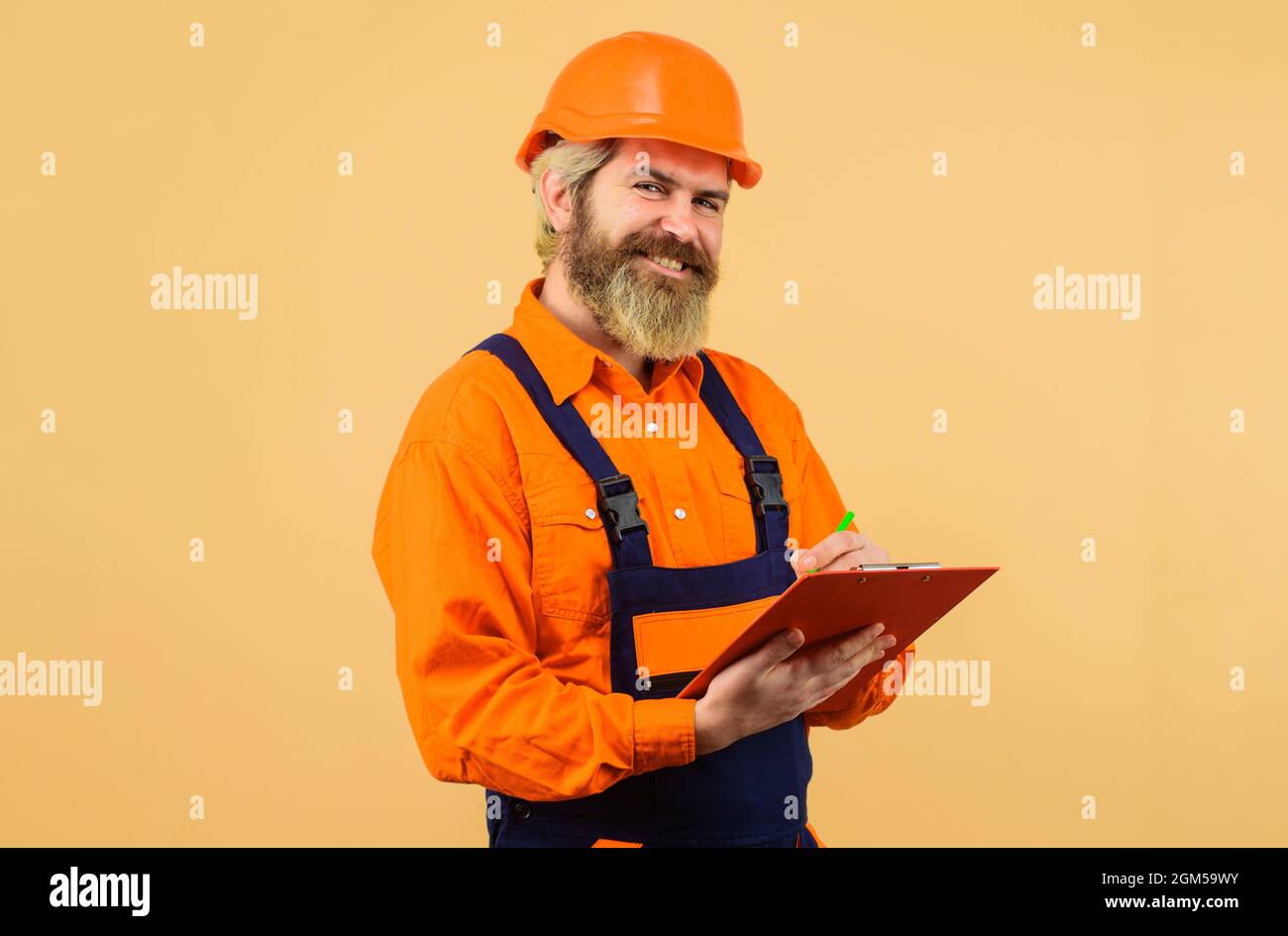 Builder in hard hat and overalls making notes in clipboard. Construction worker or repairman with folder. Stock Photo