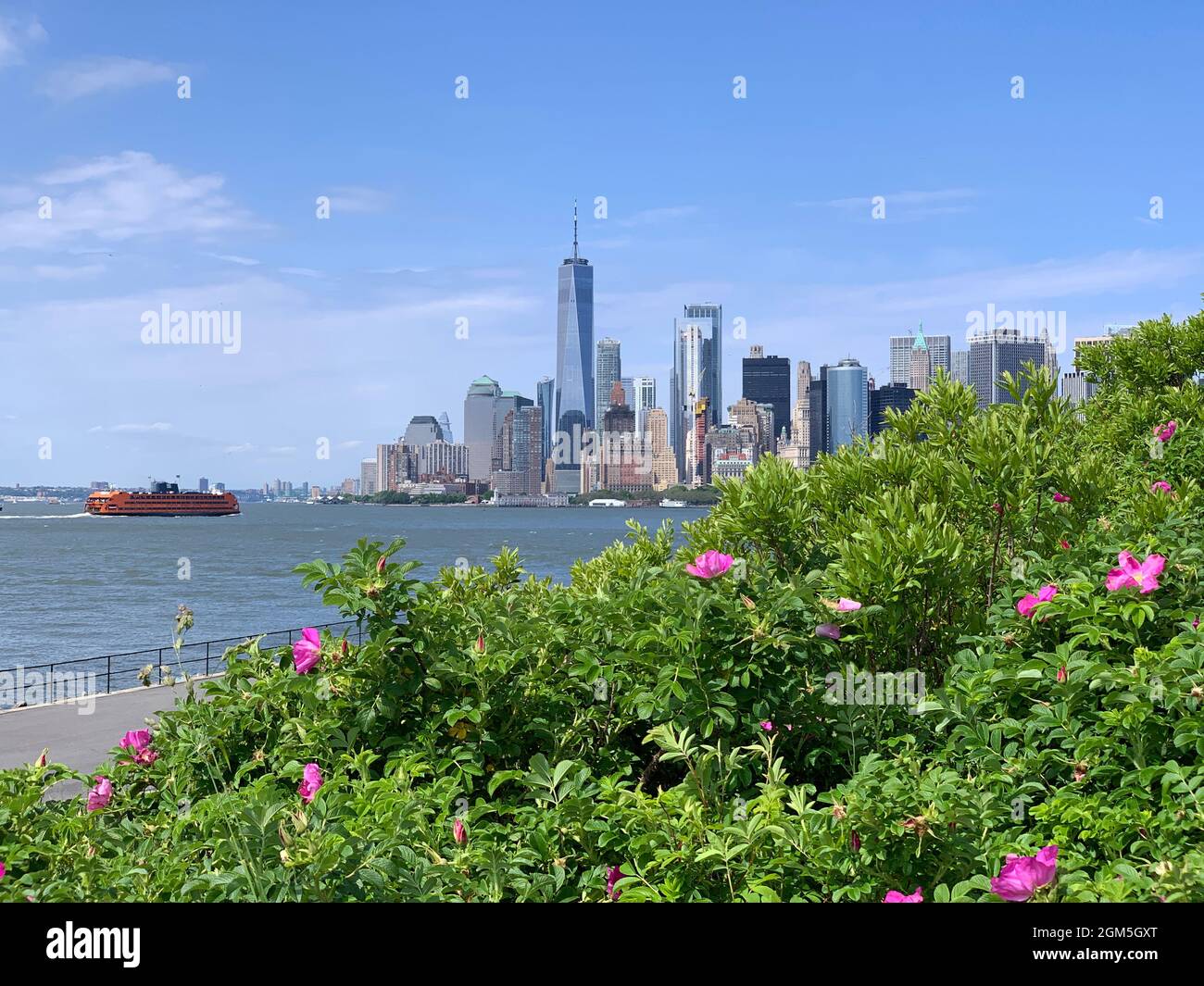 Downtown Manhattan with Staten Island ferry behind the green of Governor Island on a sunny day Stock Photo